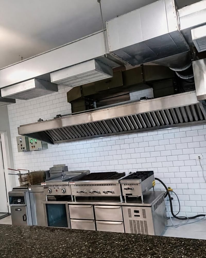Coifa de parede em inox sobre fogão e chapa de cozinha profissional